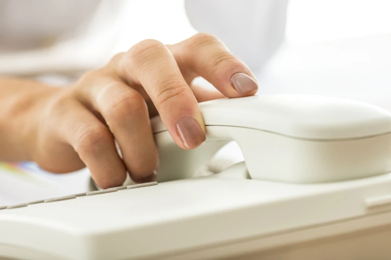 Hand nimmt weißen Telefonhörer auf einem Schreibtisch für Kundenservice und Support.