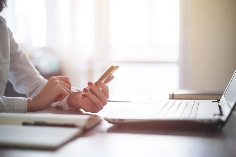 Frau arbeitet im Homeoffice am Laptop und Smartphone, digitales Arbeiten im Büroalltag.