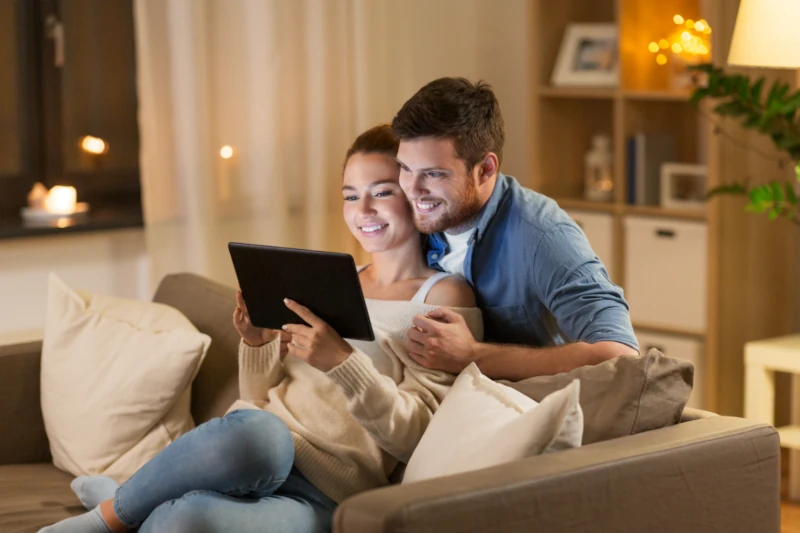 Junges Paar entspannt auf dem Sofa und surft gemeinsam mit Tablet im gemütlichen Wohnzimmer.